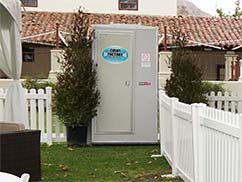 Deluxe portable toilet near Asuncion in front of white picket vinyl fencing.